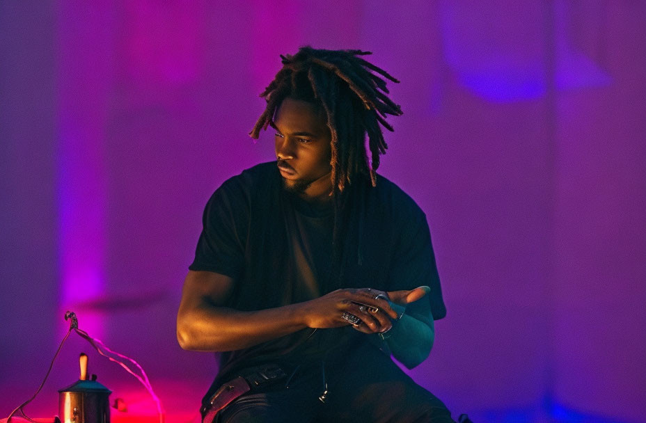 Man with dreadlocks in black shirt under soft purple lighting