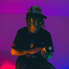 Man with dreadlocks in black shirt under soft purple lighting