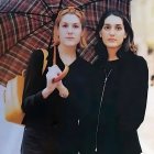 Two girls under colorful umbrella in rain with castle silhouette.