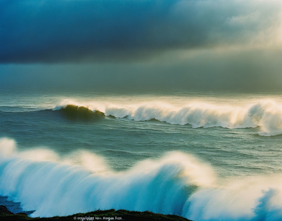 Golden light illuminates ocean waves under storm clouds on rugged coastline