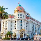 Luxurious coastal hotel with dome, palm trees, and blue sky captured in warm sunlight