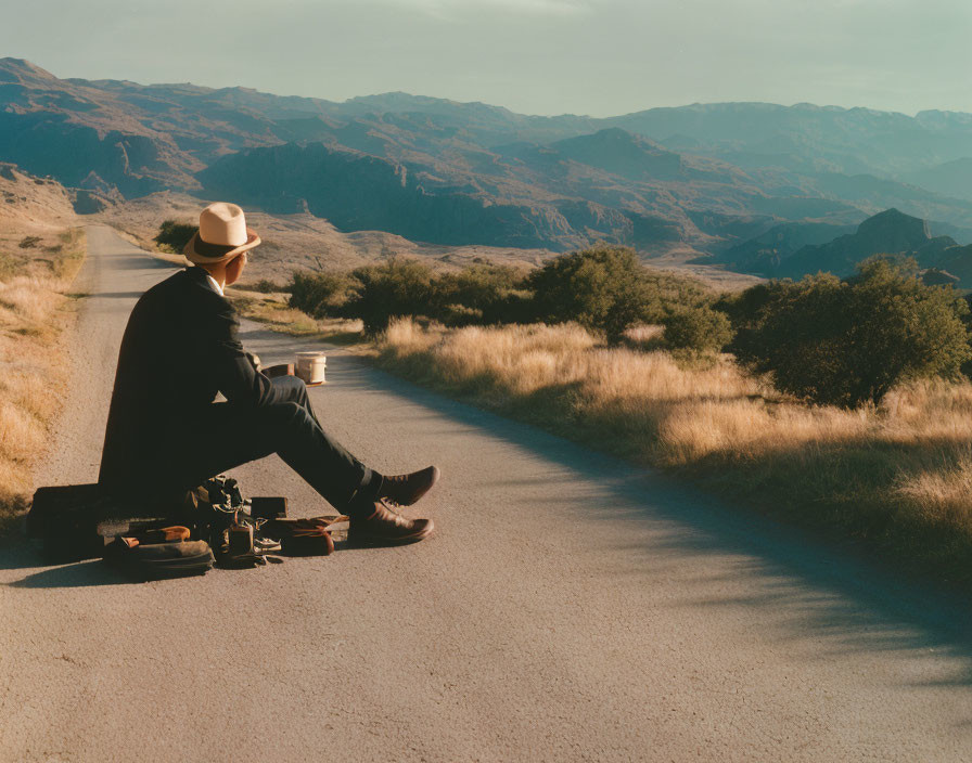 Cowboy hat person with suitcase on empty road gazing at mountain landscape