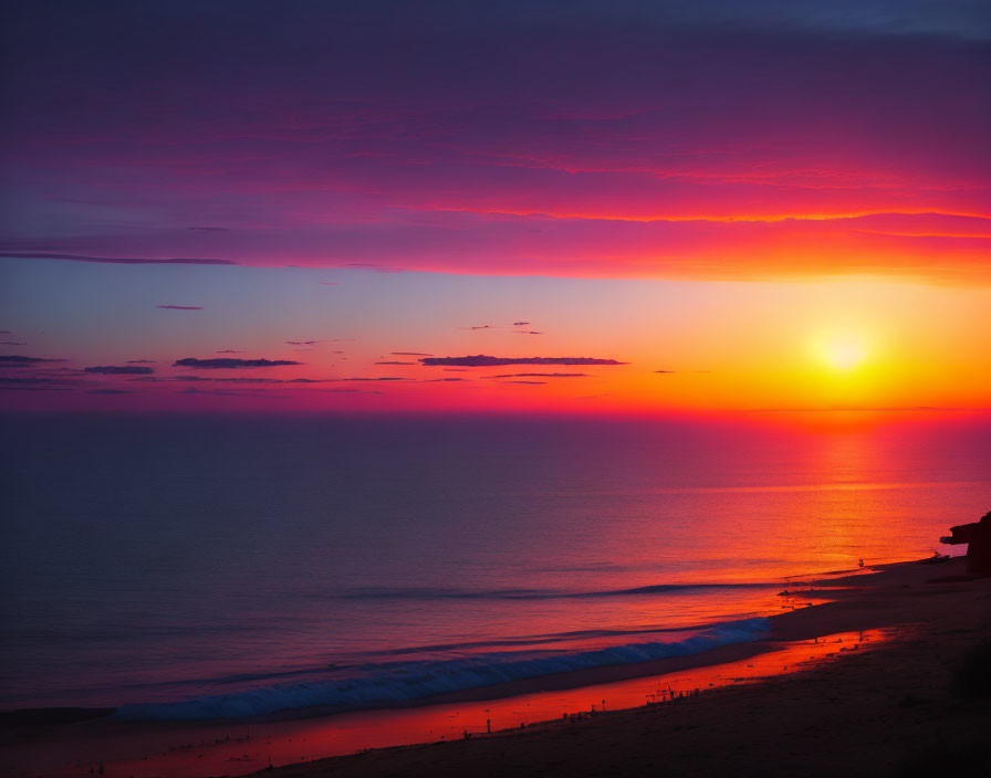 Vibrant purple and red sunset over calm ocean with silhouetted figures and gentle waves