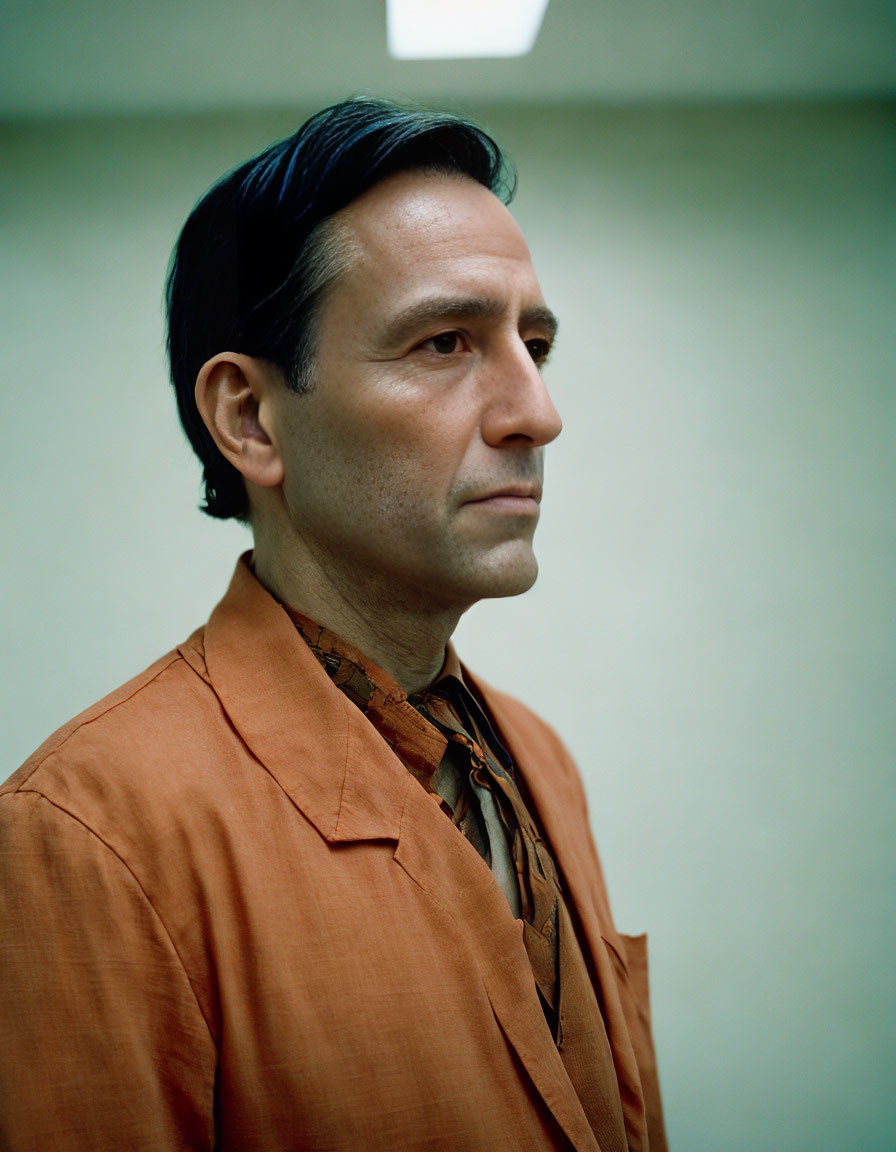 Serious man in orange shirt and patterned tie on plain background