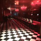 Luxurious bar with checkerboard floor, pink lights, dark walls, and purple bar stools.