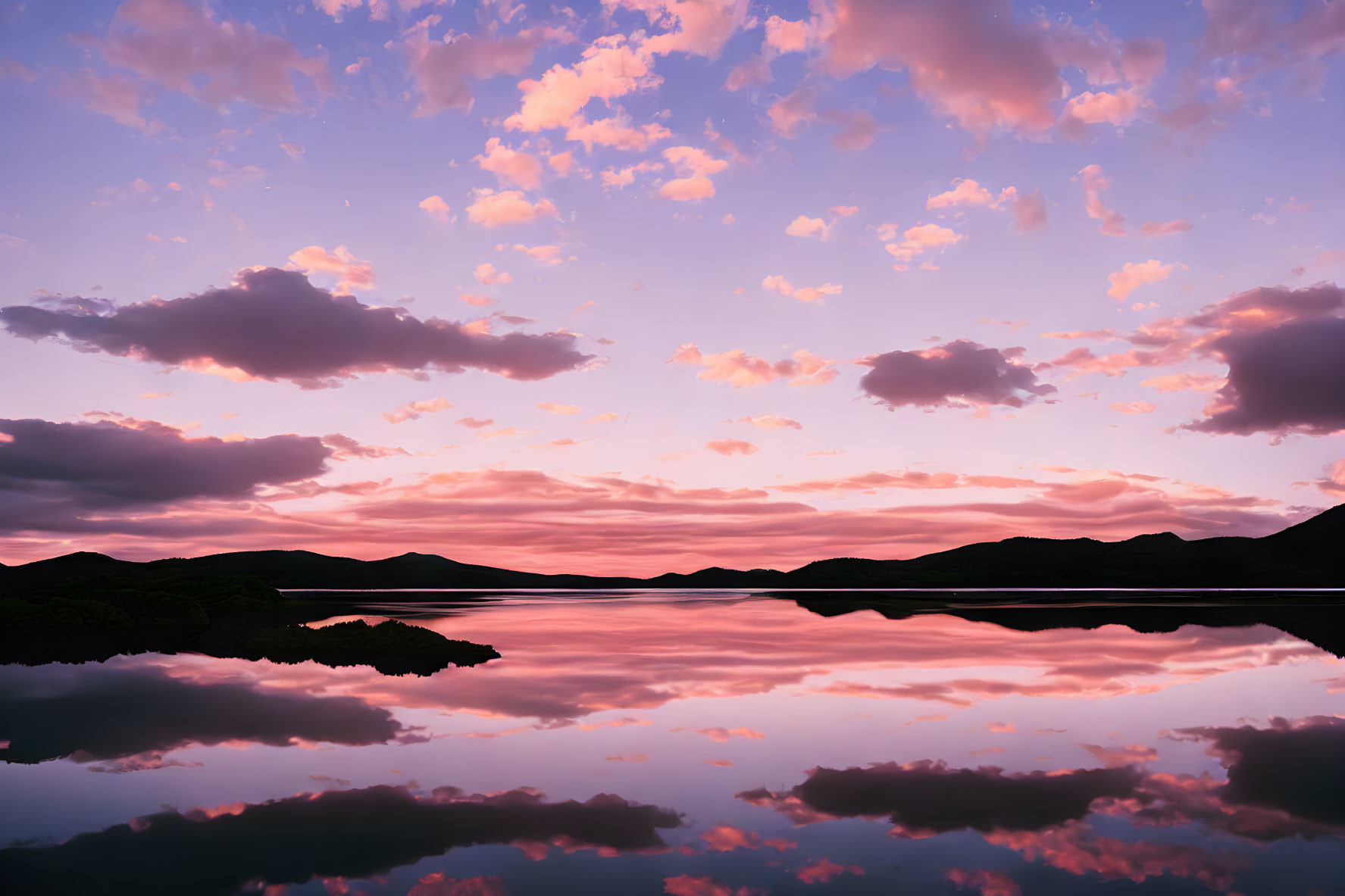Tranquil twilight scene: pink and purple clouds reflected on serene lake.