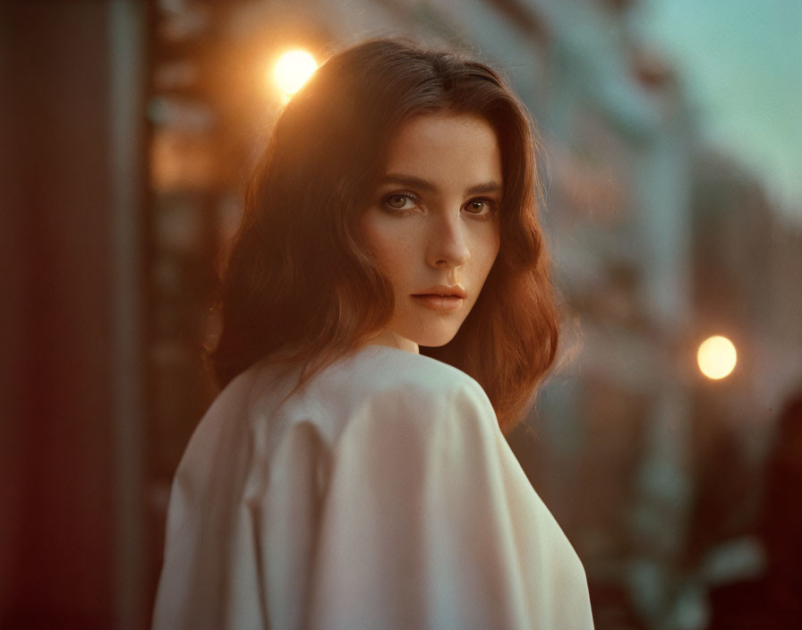 Brown-haired woman with intense gaze in warm bokeh lights at dusk