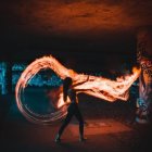 Fantasy armor-clad woman controls fire in dim cave with glowing plants