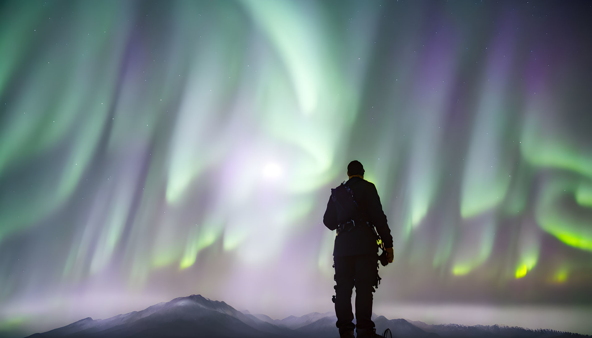 Silhouetted observer under aurora borealis and snowy mountains