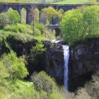 Viaduct with multiple arches over green valley and waterfall.