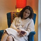 Woman in white knit dress sitting in blue chair with geometric shadows background