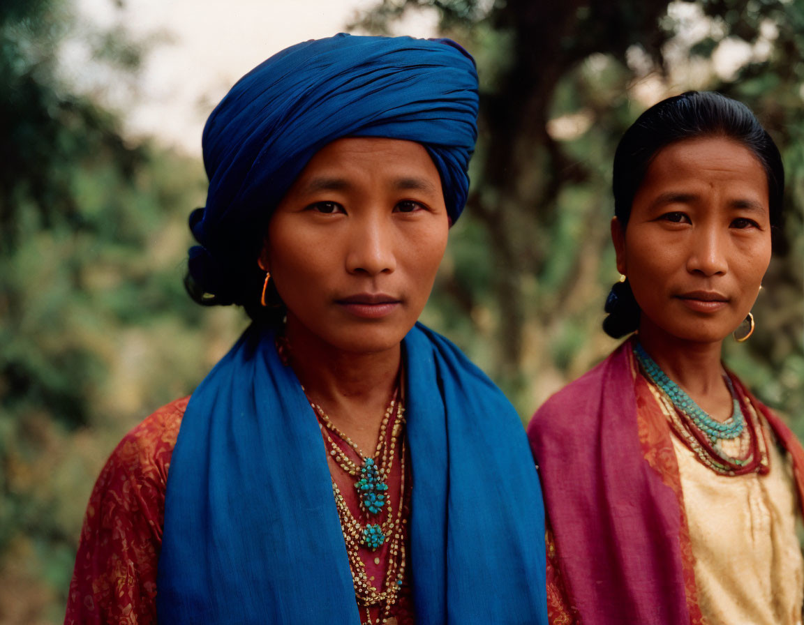 Two women in traditional headscarves and colorful attire outdoors with focused expressions