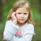 Young girl with floral headband in lush greenery holding pink rose