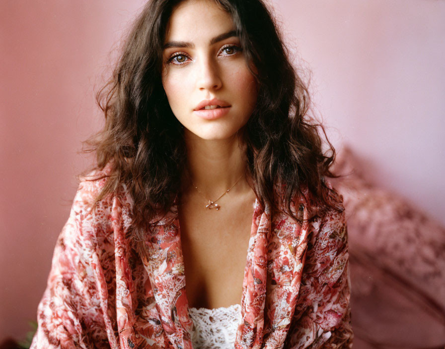 Dark-haired woman in floral kimono and lace top in softly lit pink room