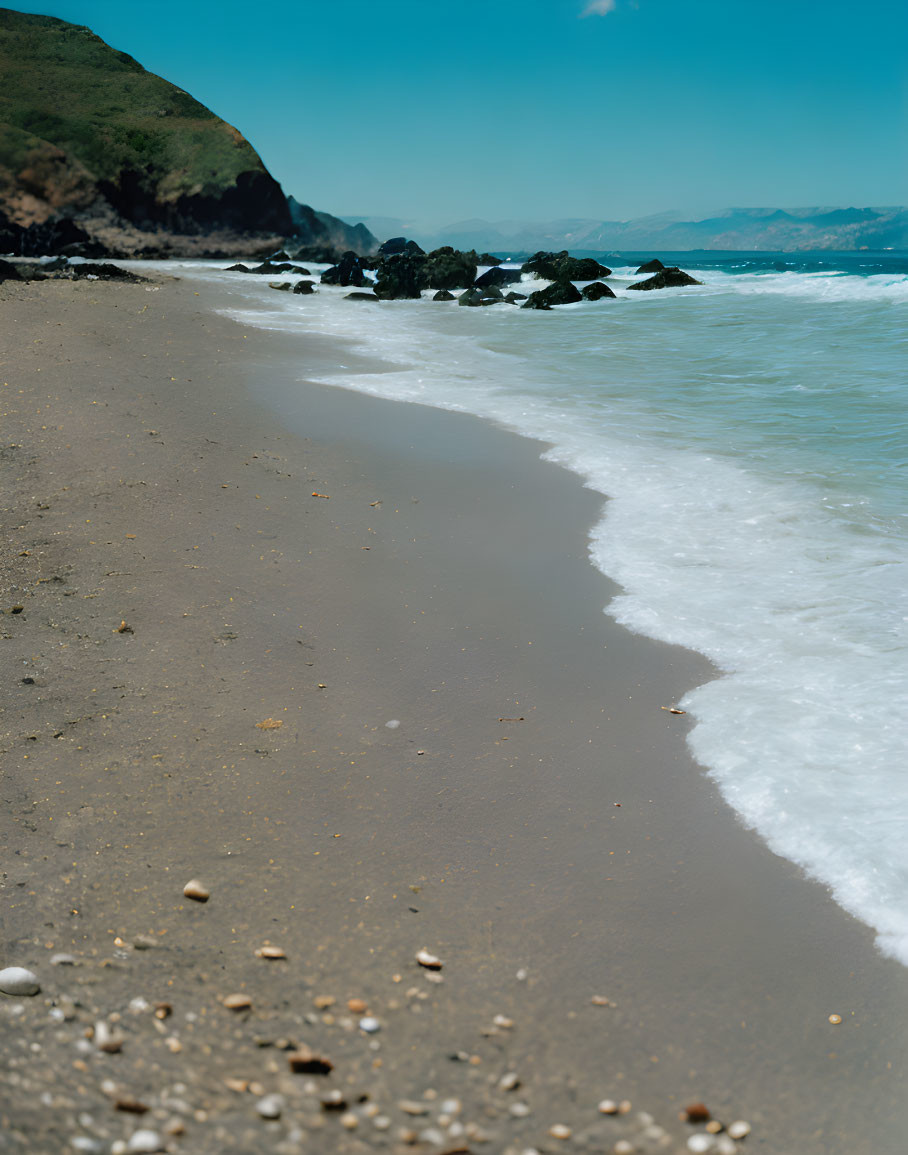 Tranquil beach scene with gentle waves and rocky outcrops