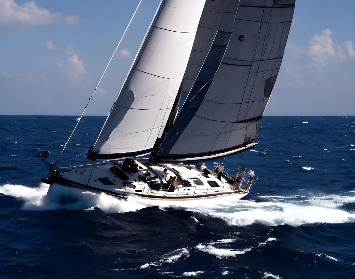 Sailboat with multiple open sails heeling over in blue ocean waves