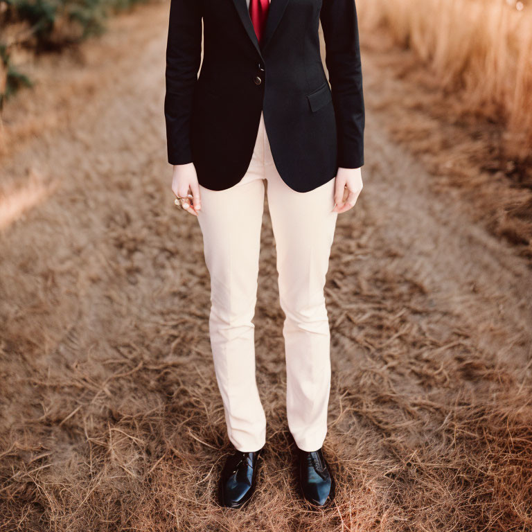 Person in black blazer, white pants, red shirt, and black shoes in a field