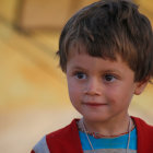 Smiling toddler with curly hair in red jumper on golden background