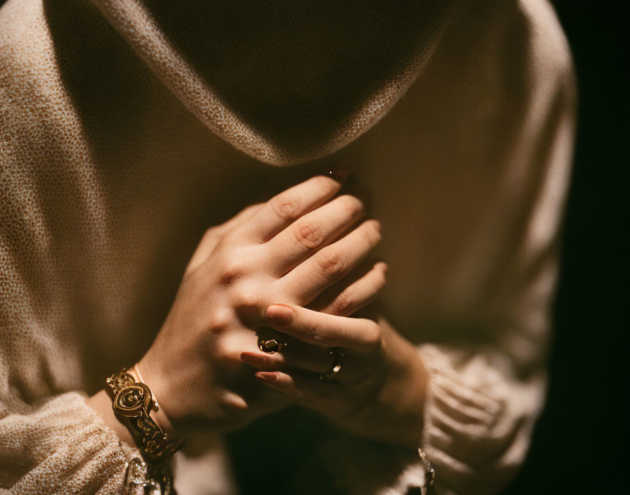 Person's crossed hands with watch and rings against dark background with soft-focus texture.