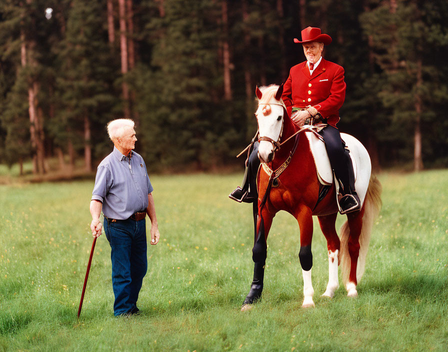 Red jacket person on horse talking to standing person with cane in grassy field