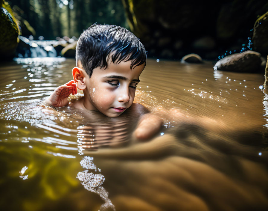 Boy swimming in forest creek under dappled sunlight