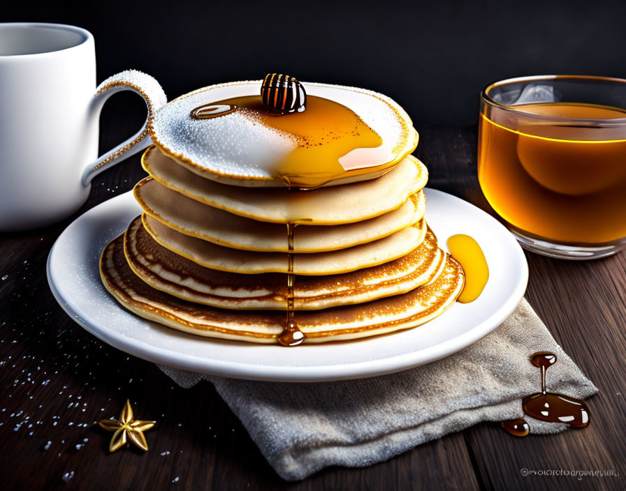 Golden pancakes with honey, tea, and anise stars on dark wooden table