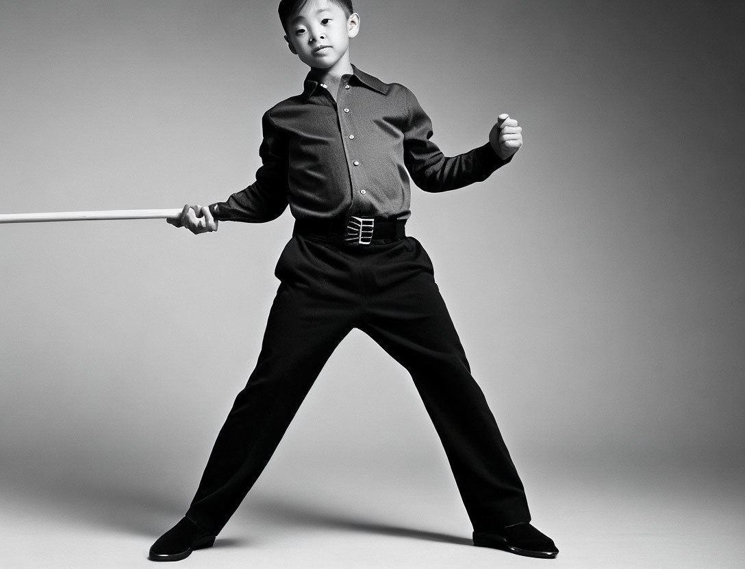 Confident young boy in martial arts pose with staff on grey background