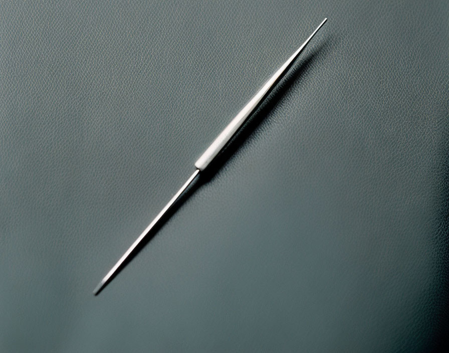 Metallic sewing needle with thread eye on grey surface