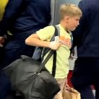 Young boy in yellow shirt walking with person carrying suitcase in crowded area