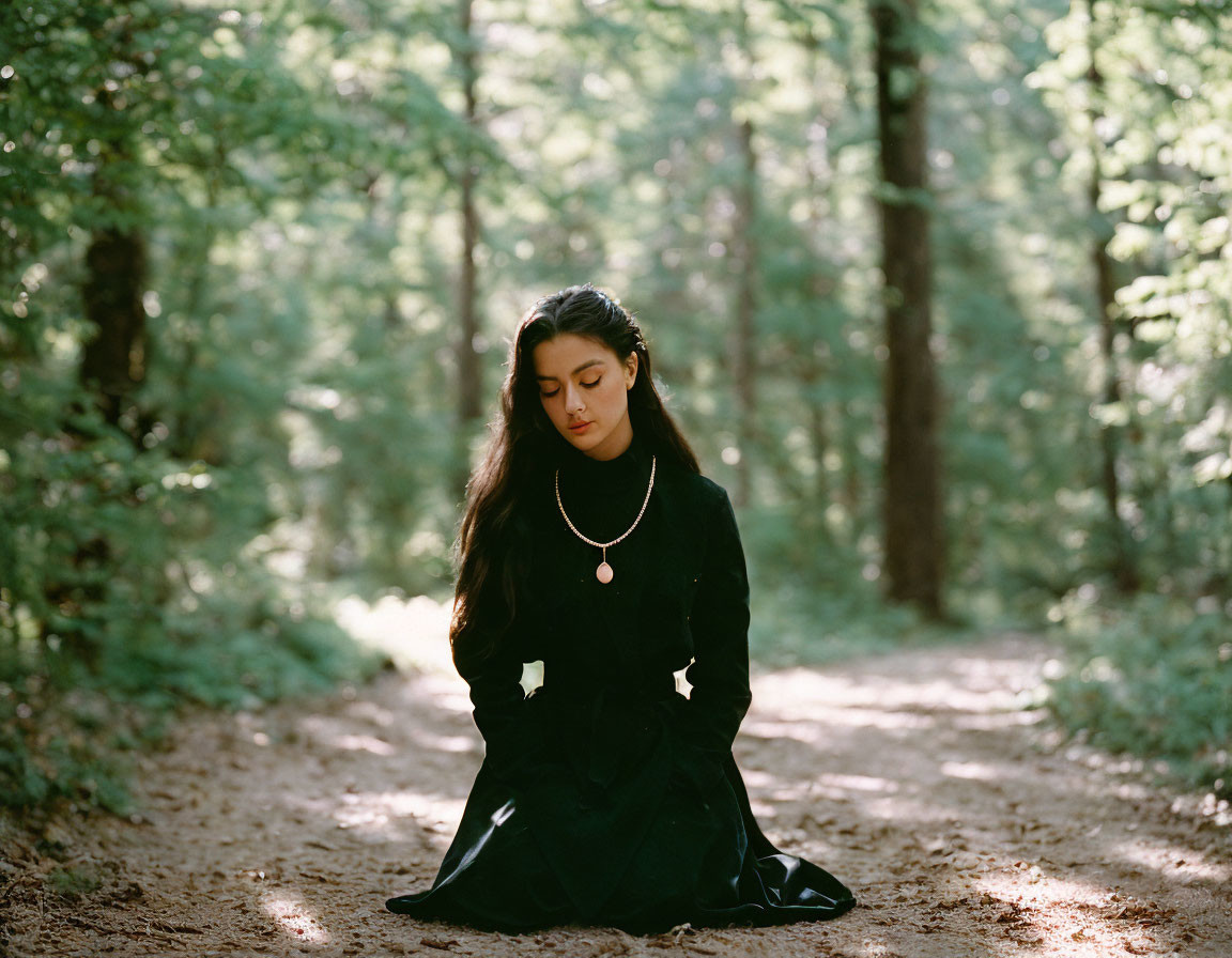 Woman in Black Dress Sitting on Forest Path Surrounded by Tall Trees