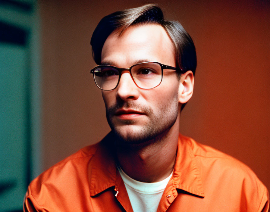 Bearded man in glasses wearing orange shirt against blurred backdrop