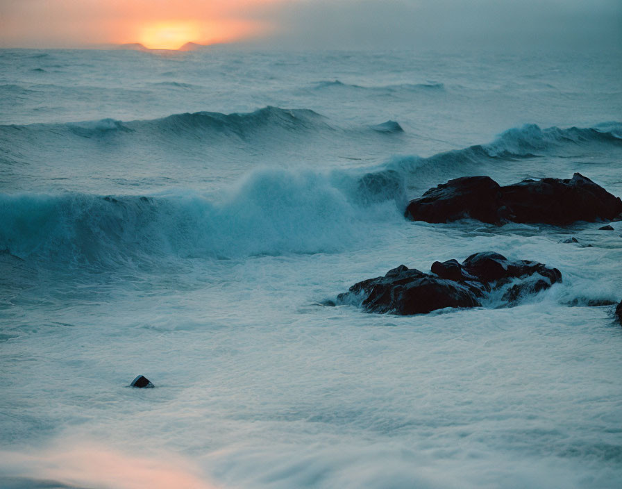 Sunset waves crashing against rocks with orange glow and sea mist.