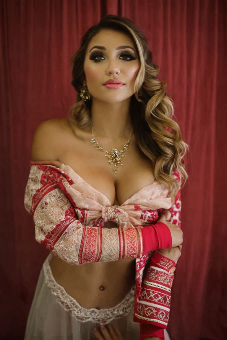 Elegant woman in off-shoulder garment with makeup and jewelry against red backdrop