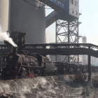 Vintage steam locomotive chugging near industrial tracks and concrete structures