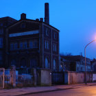 Industrial facility with pipes and tanks in blue twilight, showcasing cylindrical structure and smokestacks in dusky