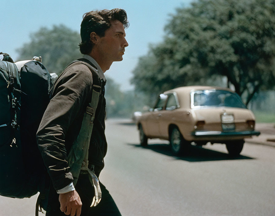 Man with backpack standing by road as vintage car drives by