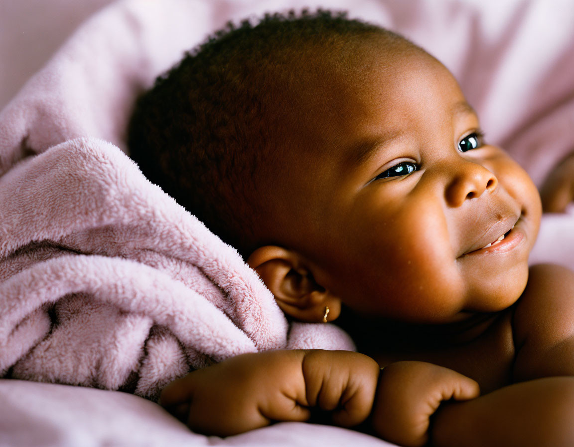 Smiling baby with chubby cheeks on pink blanket gazes upward