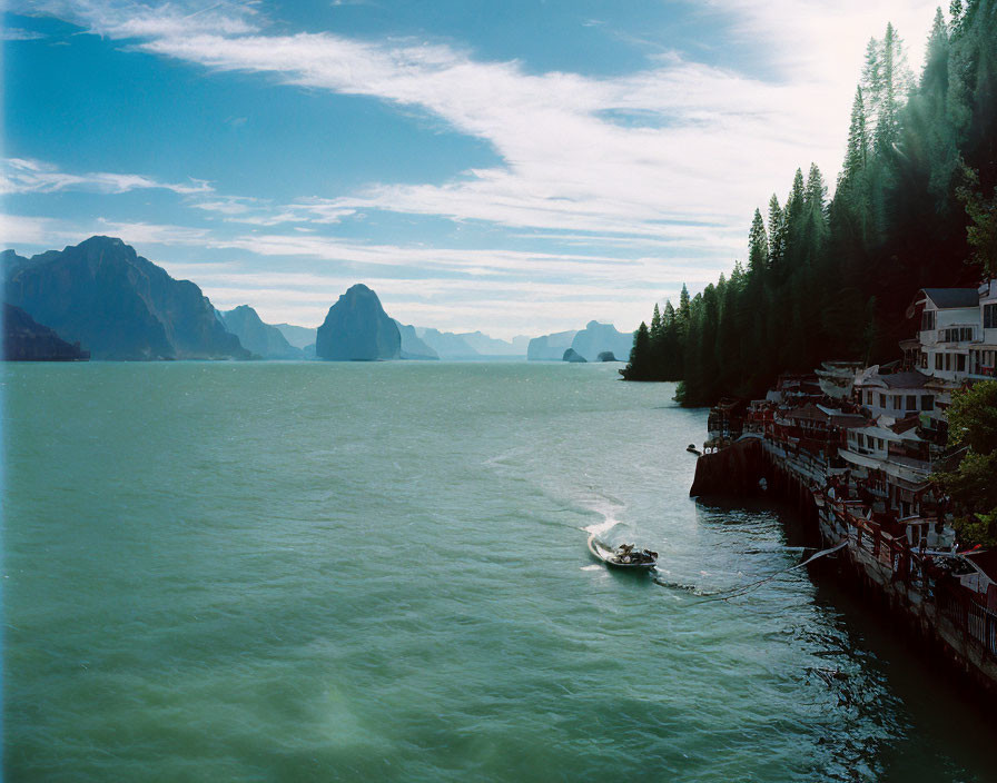 Scenic boat sailing on serene green-blue lake with mountains and treelined coast.