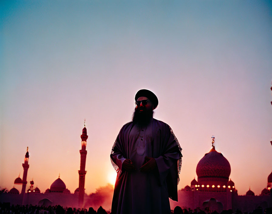 Bearded man in traditional attire at mosque silhouette sunset.