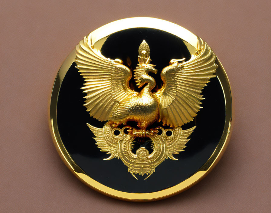 Golden Ornate Mythical Bird Emblem on Black Circle Against Tan Surface