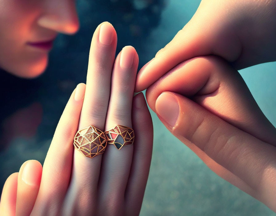 Geometric heart-shaped rings on hands touching tenderly with blurred face in background