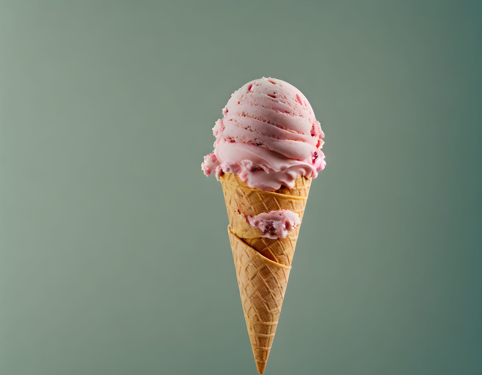 Strawberry ice cream scoop with sprinkles in waffle cone on teal background