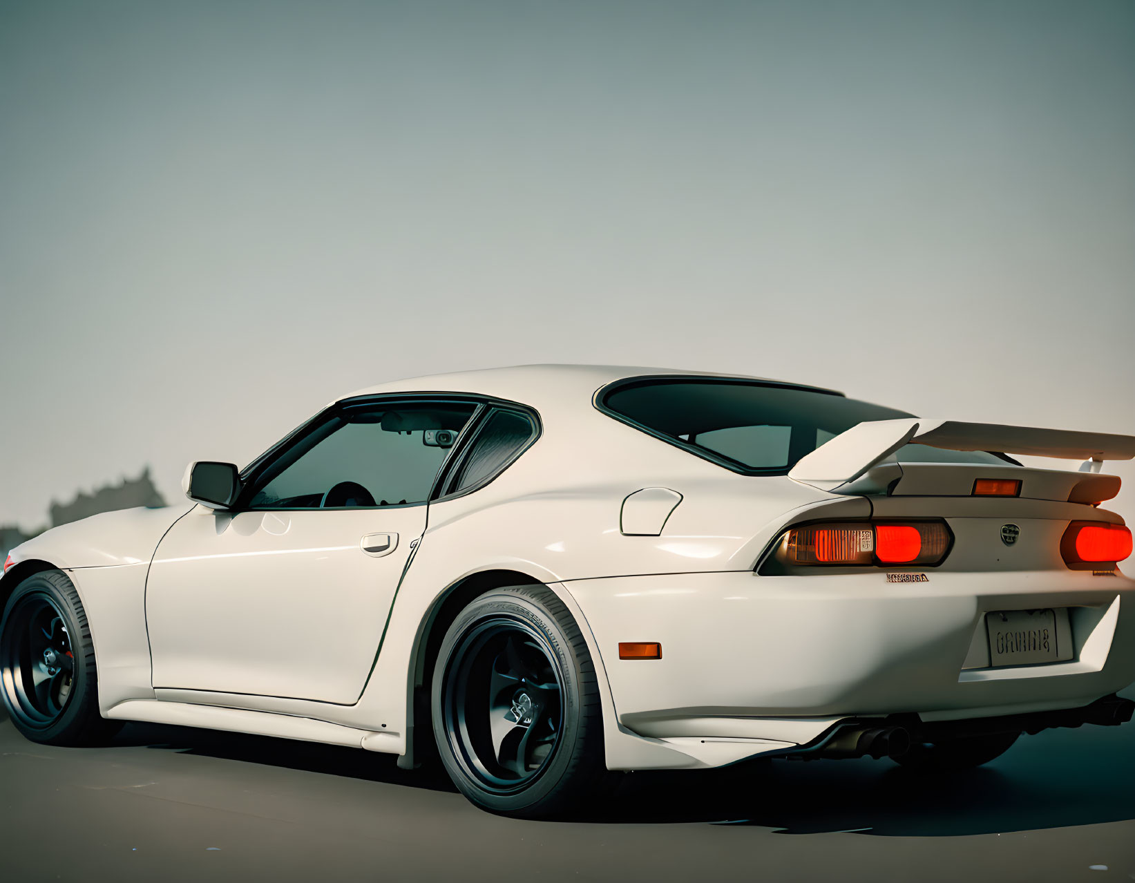 Vintage white sports car with rear spoiler and black wheels under clear sky