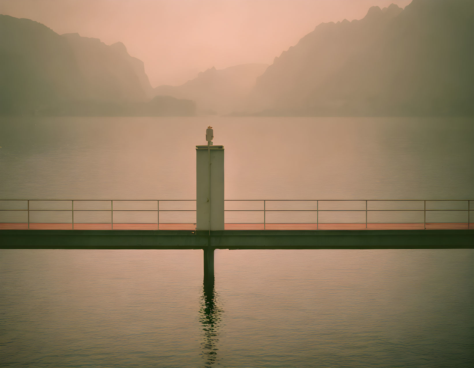 Tranquil landscape with lighthouse, pier, calm waters, misty mountains, and golden sky