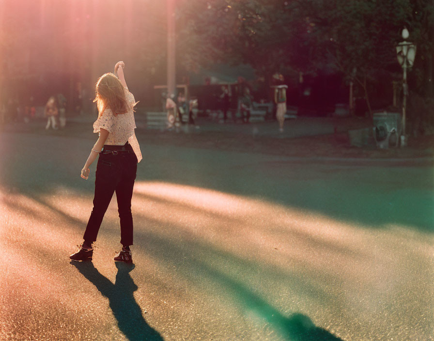 Person dancing in sunlit haze on street with blurred passersby in background.