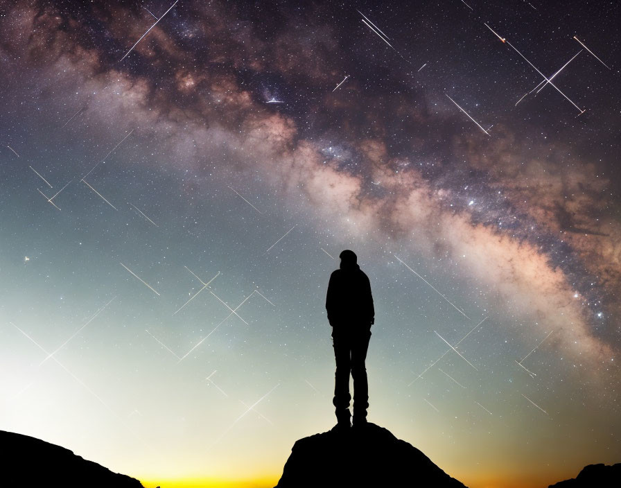 Person's silhouette on hilltop under starry night sky with Milky Way and meteor shower streaks