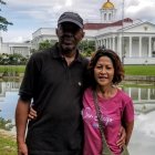 Man and woman posing by pond with gazebo and greenery