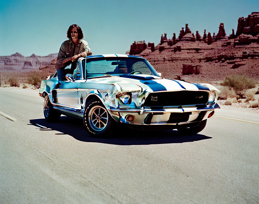 Person in sunglasses on hood of classic Shelby GT350 Mustang in desert landscape