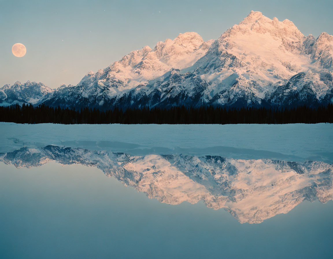 Snow-covered mountain range under full moon's reflection in calm lake at twilight