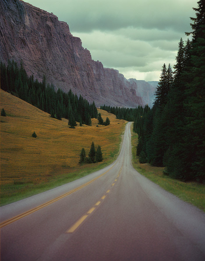 Serene landscape with road, lush greenery, cliff, and cloudy sky